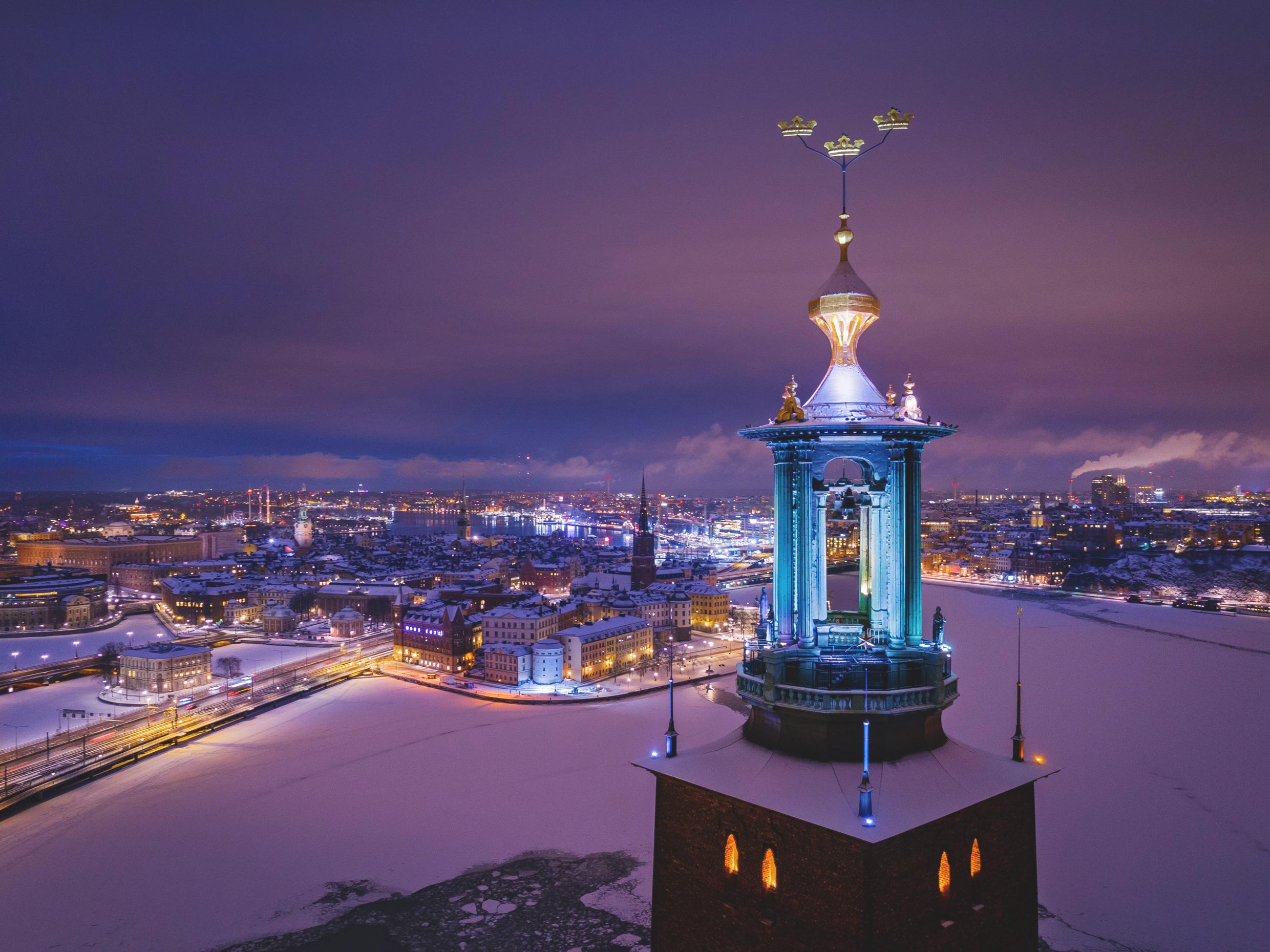 Illuminated Stockholm City Hall tower overlooking the snowy cityscape and frozen waterways at night, showcasing Stockholm’s winter charm.