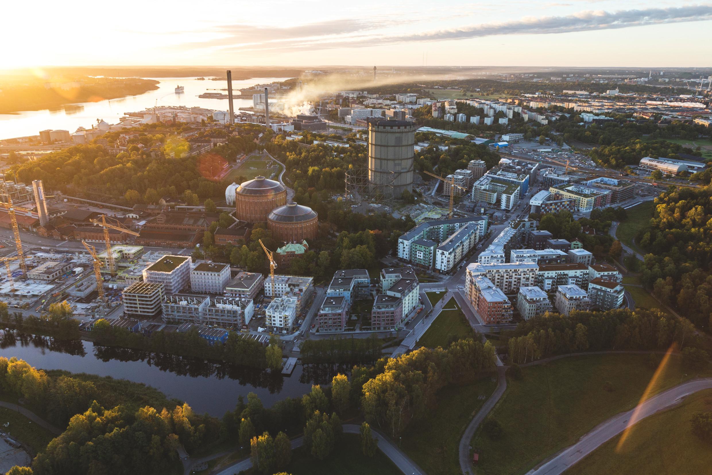 Aerial view of a Stockholm district at sunrise, showcasing sustainable urban planning with modern residential buildings, green spaces, and industrial structures.