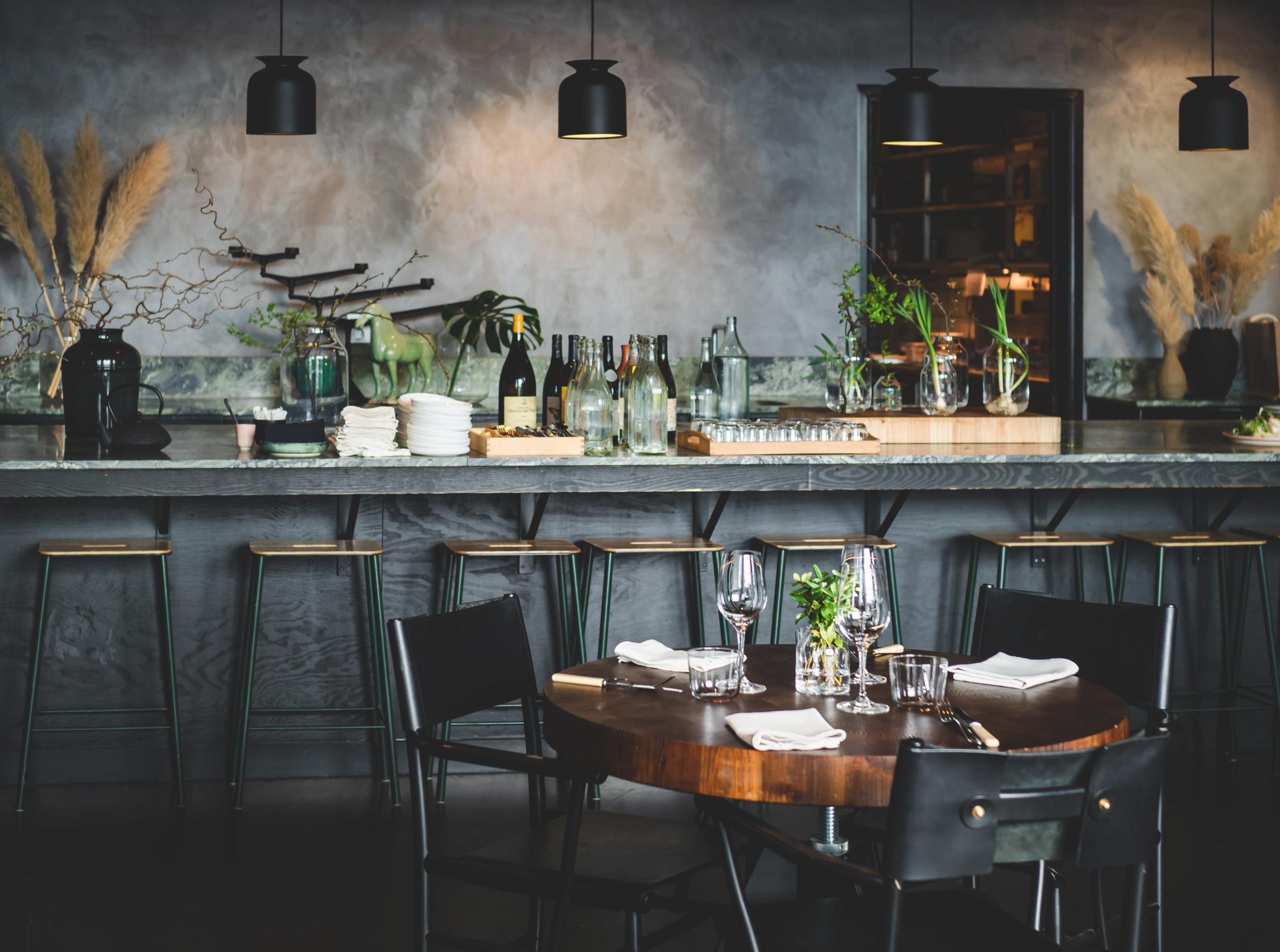 Modern Stockholm restaurant interior with a round wooden table set for dining, a stylish bar in the background, and minimalist decor.