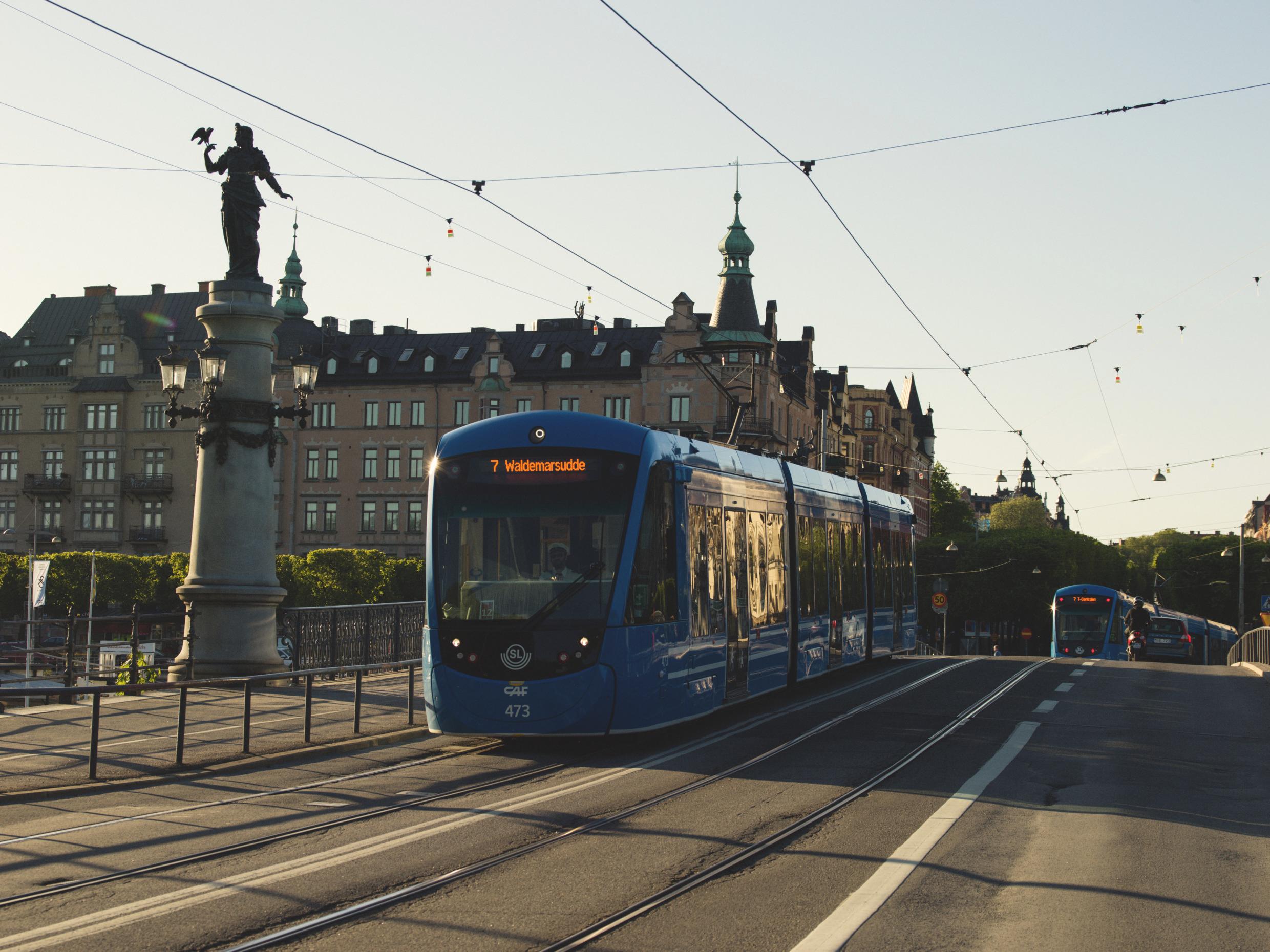 Blue tram crossing a bridge in central Stockholm, surrounded by historic architecture and city landmarks during sunset.