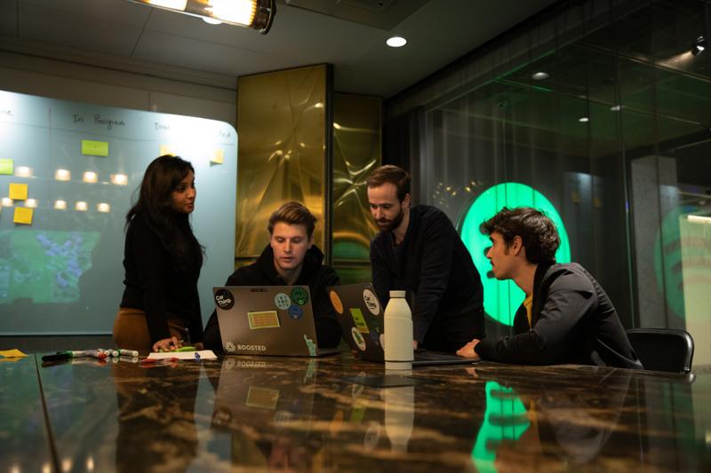 Group of professionals collaborating at a marble table in a modern Stockholm office, brainstorming ideas with laptops and whiteboards.